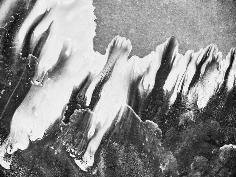 Black-and-white aerial photograph of Kati Thanda–Lake Eyre showing flowing salt and water formations from above, resembling abstract brushstrokes and organic shapes etched into the vast desert landscape.