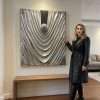 Large silver 3D wall sculpture titled Silver Veils by Samaa, featuring deep metallic fabric-like folds gathered around a central textured sphere on a dark background.